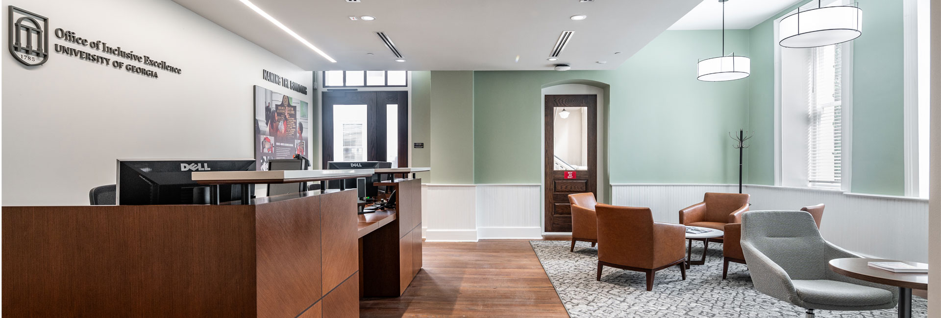 reception of the Office of Inclusive Excellence at the University of Georgia with wood desk mint green accent wall with white wainscoting wood floors and a seating area with brown and grey chairs renovation by Ajax Building Company